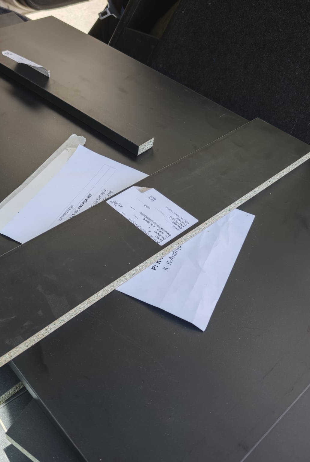 Pre-cut black cabinet panels for Project Vulcano stacked in the back of a car, with the cutting list papers on top