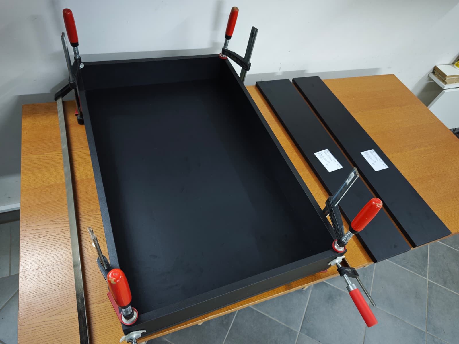 Black panels for the dartboard section of the dartR Vulcano cabinet being assembled with clamps on a workbench