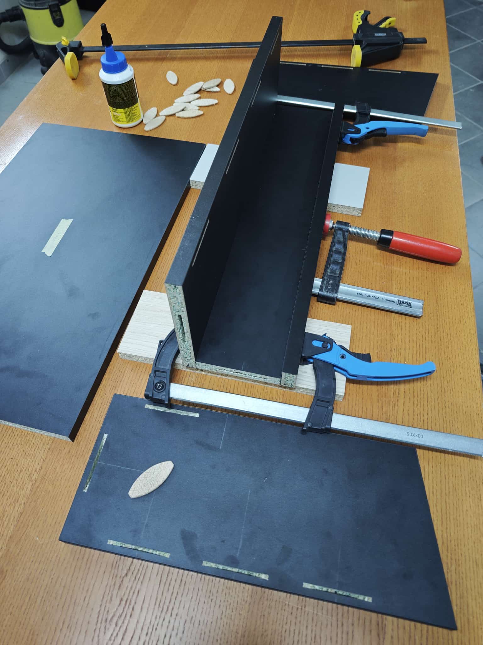Black panels, biscuits and glue laid out on the workbench for the Vulcano top section
